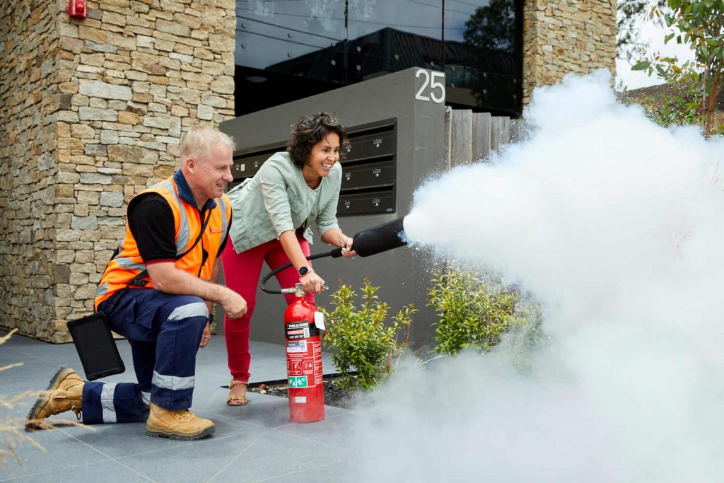 A Fire and Wire technician shows a building resident how to use a fire extinguisher